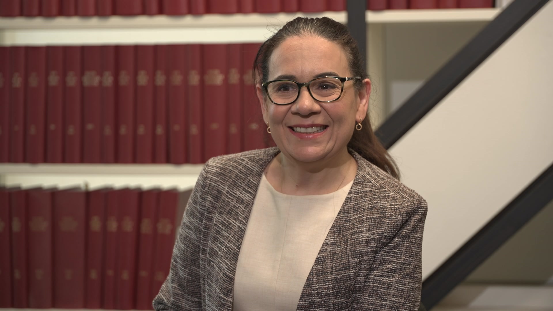 Marissa Mackie tem longos cabelos castanhos presos para trás e usa óculos