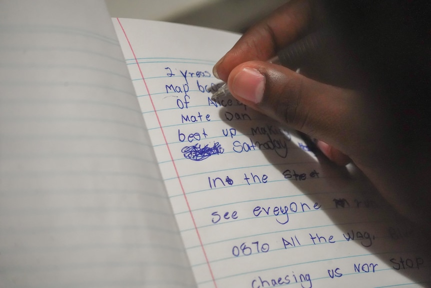A hand writes on a notebook