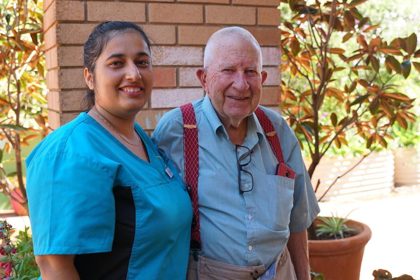 A nepalese woman in aged care uniform next to an elderly man