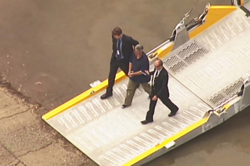Aerial view of two plain-clothes detectives escorting Steven Mark John Fennell ashore from a barge