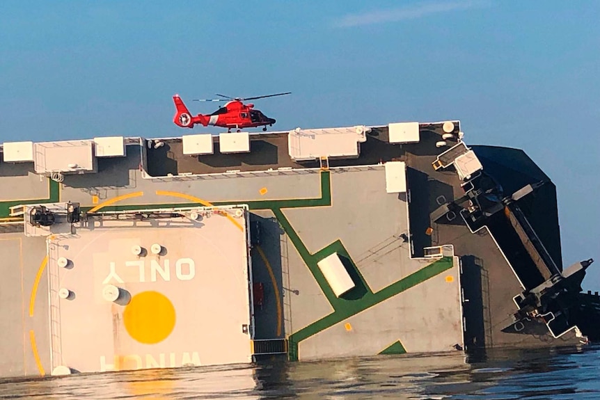 A red helicopter lands on a capsized ship.