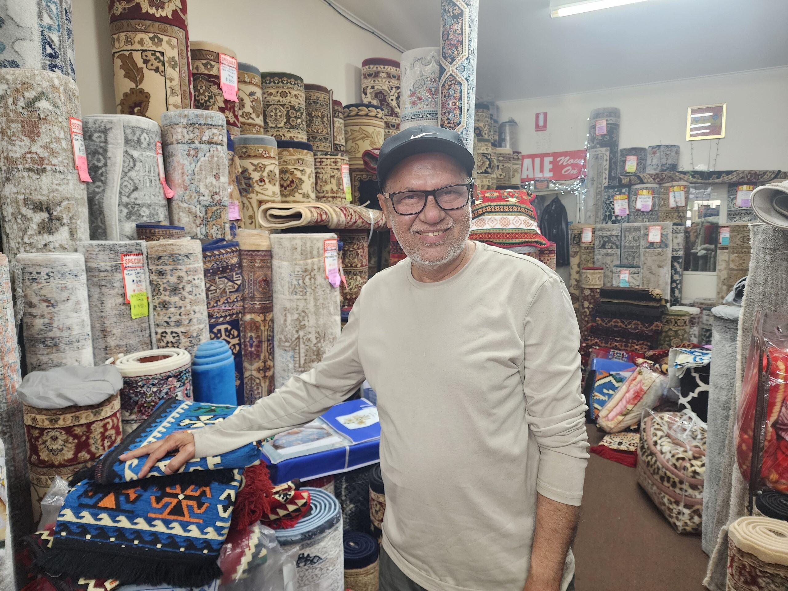 An older man in his rug shop with carpets behind him