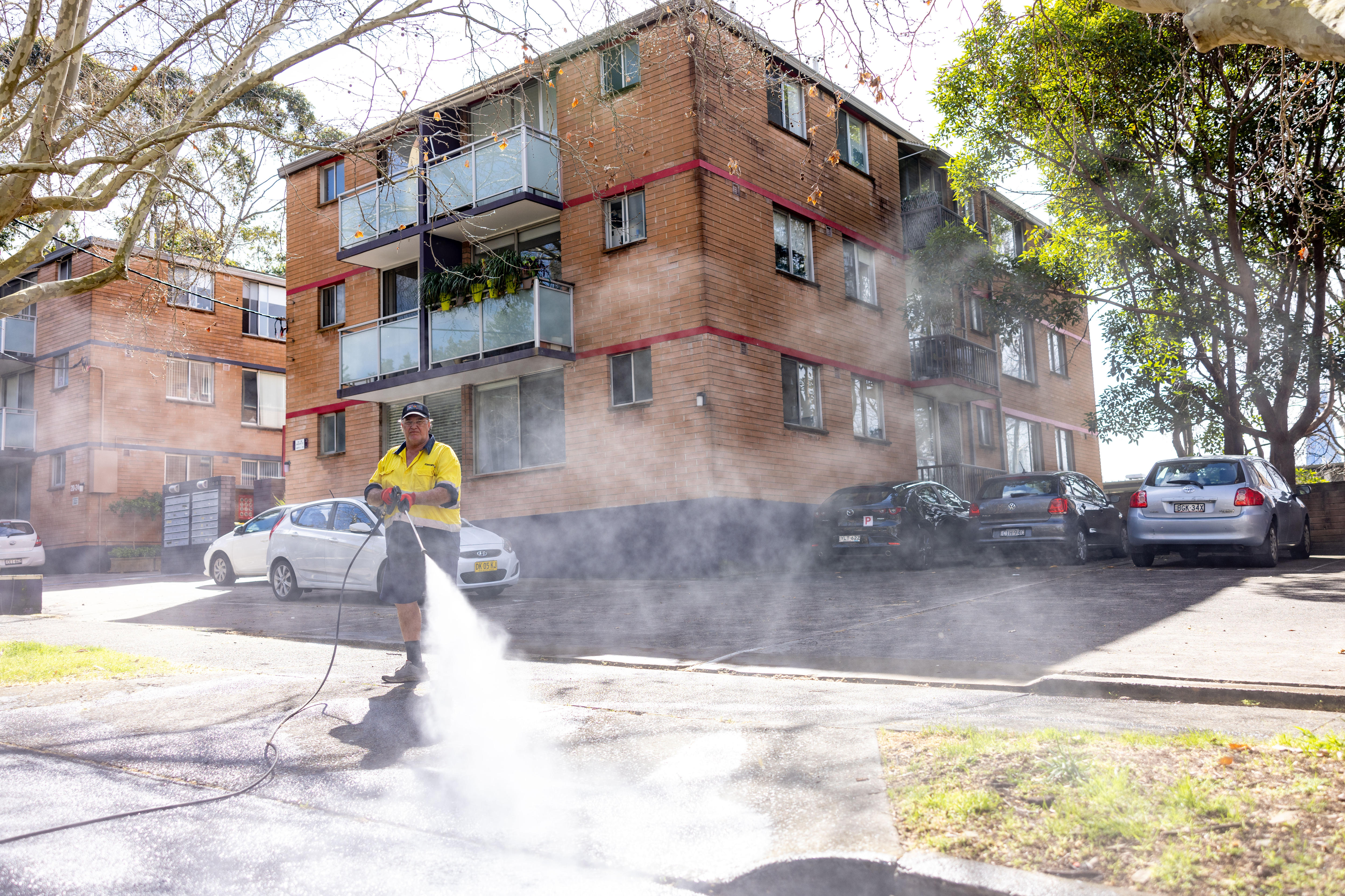 a man in a yellow shirt pressure hoses down a driveway in front of an apartment