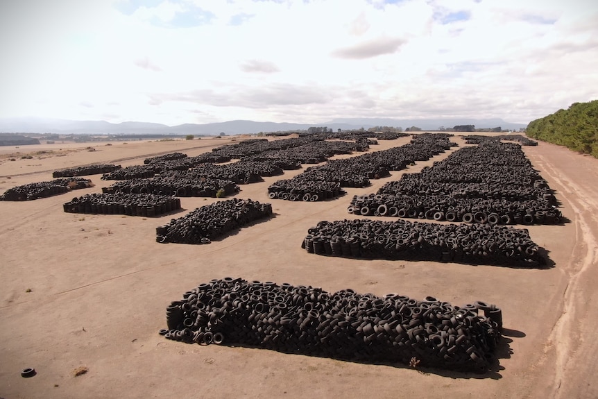 Thousands of used tyres in piles spread out over a brown landscape.