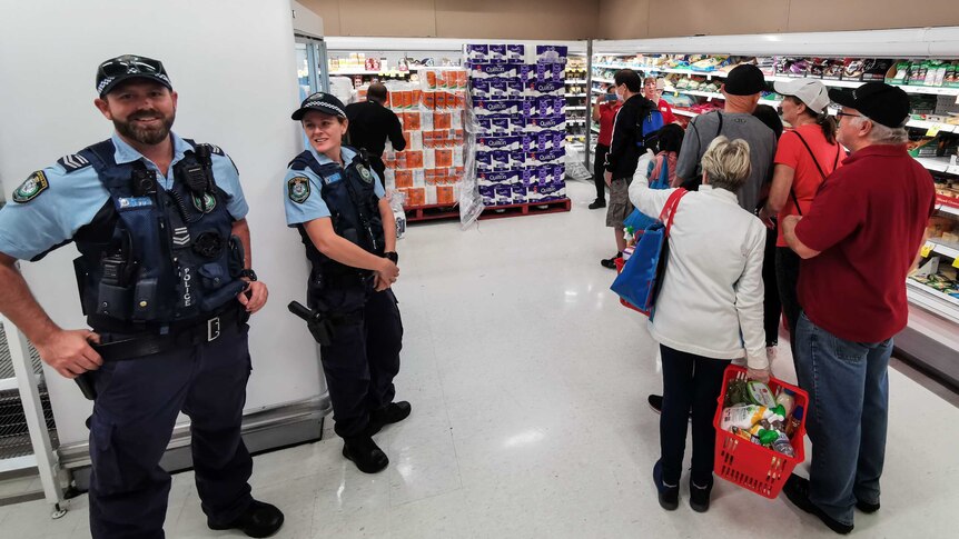 Two police officers watch a line of customers in a shop waiting to buy toilet paper