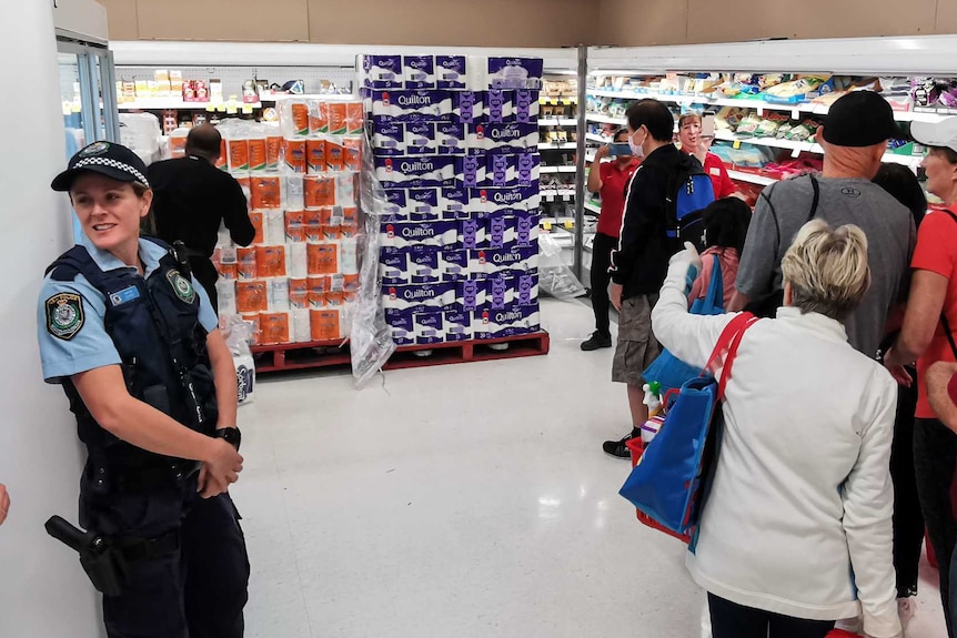 Two police officers watch a line of customers in a shop waiting to buy toilet paper