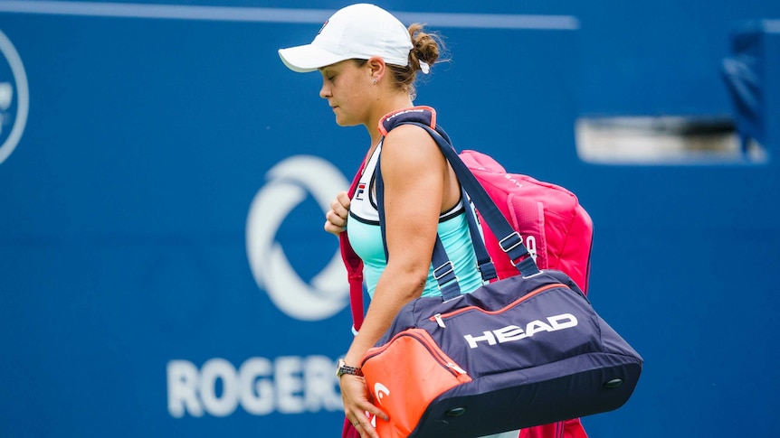 A tennis player walks off the court, eyes down, carrying her bags after a loss.