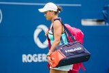 A tennis player walks off the court, eyes down, carrying her bags after a loss.