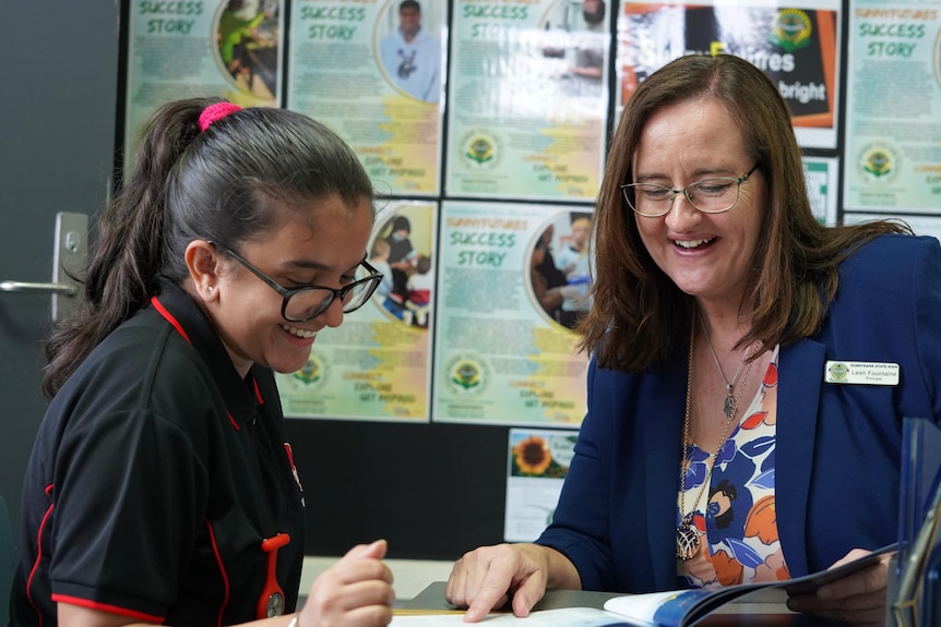 A young woman sits with Leah Fountaine reading from a booklet, both smiling. 