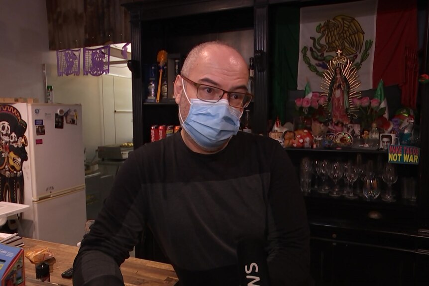A man in a blue surgical mask with glasses stands behind a bar