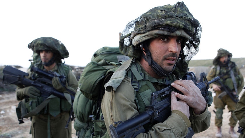 A soldier in camouflage holds a gun to their chest. 