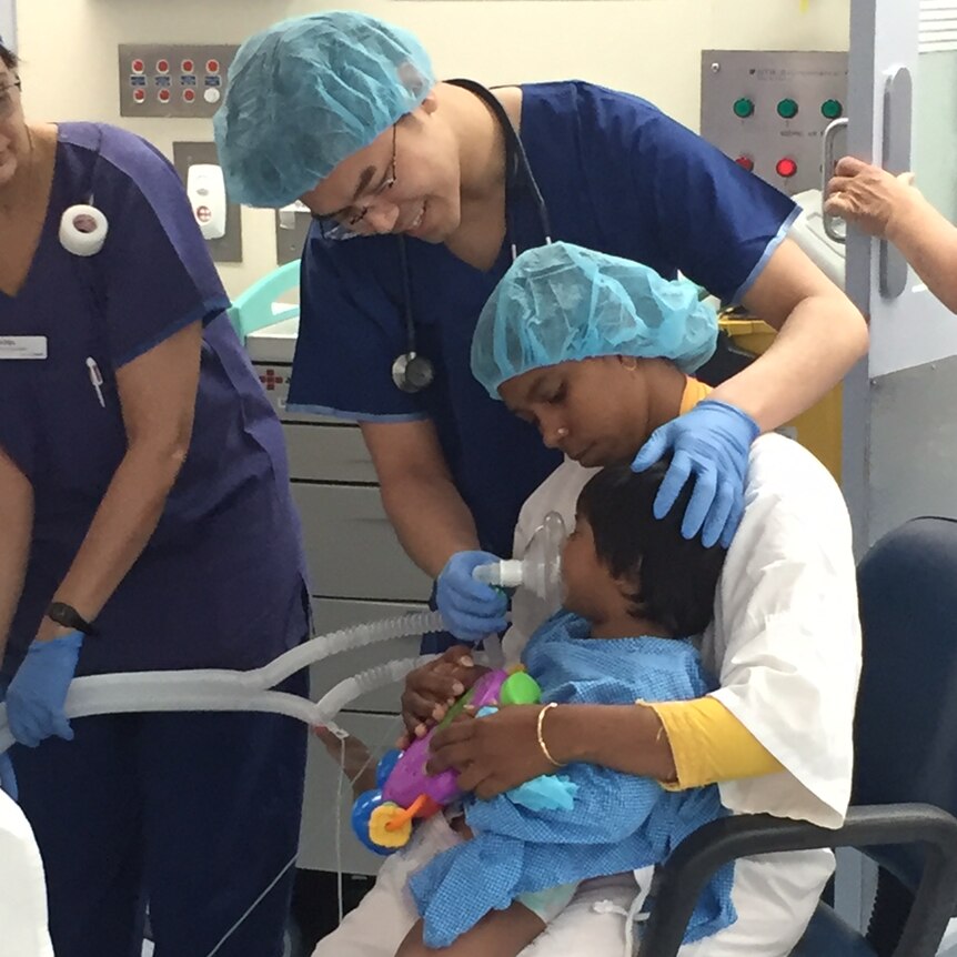 Choity is held by her mum as doctors place a breathing apparatus on her mouth in surgery.