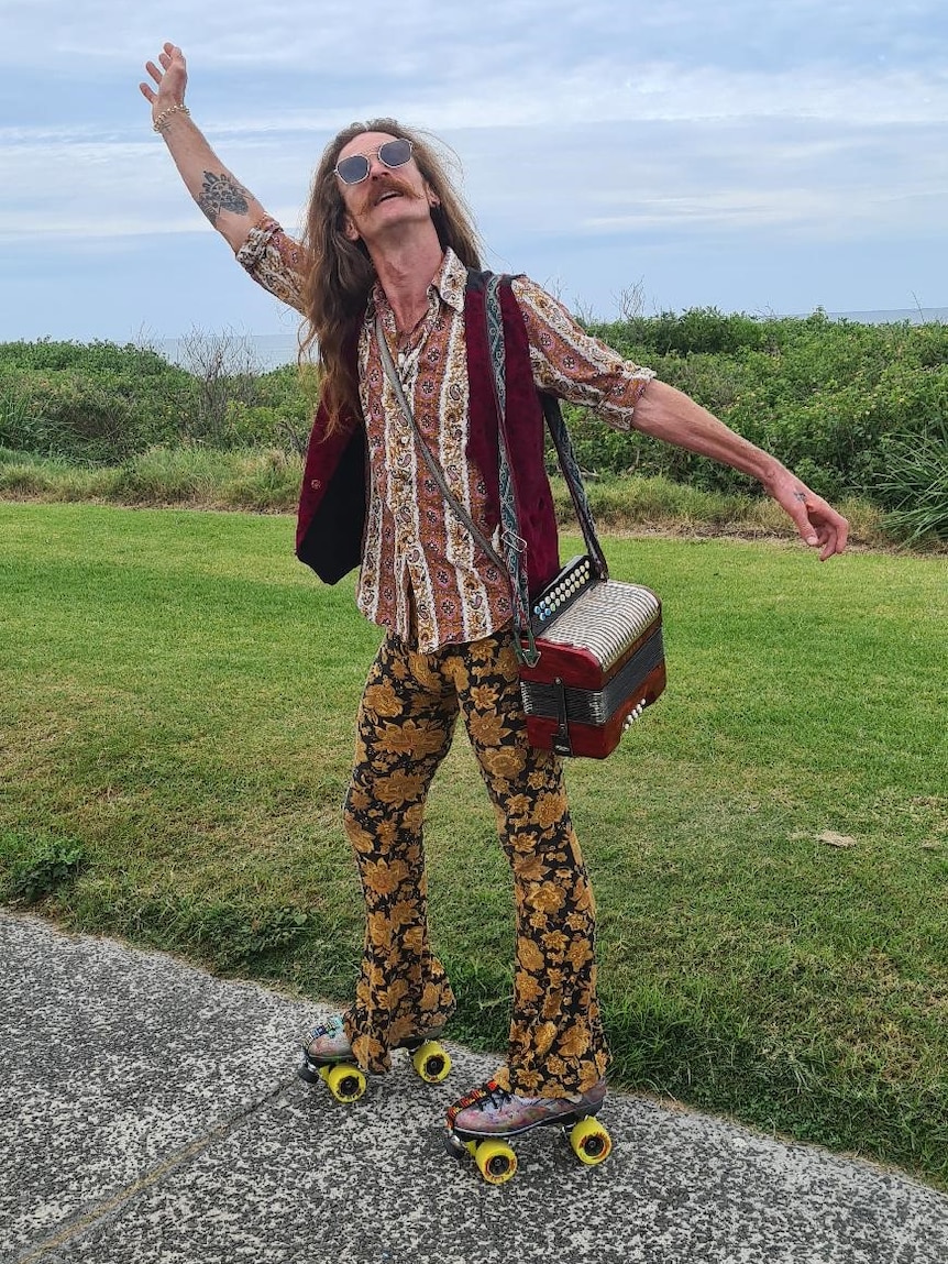 A man with long red hair wearing sunglasses and a red striped shirt and red vest,