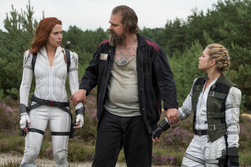 David Harbour firmly holds the arms of Scarlett Johansson and Florence Pugh, who are standing on either side of him