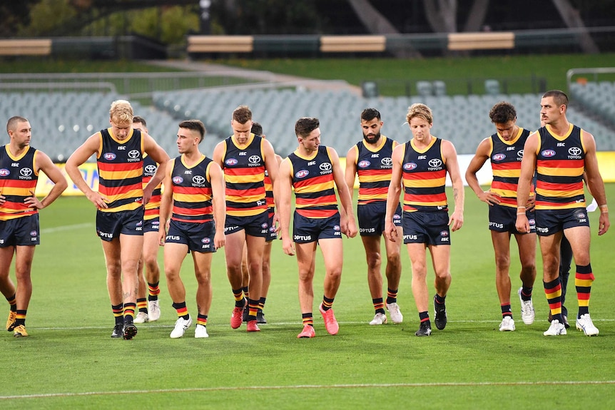Adelaide Crows players look dejected as they walk off the field in front of empty stands