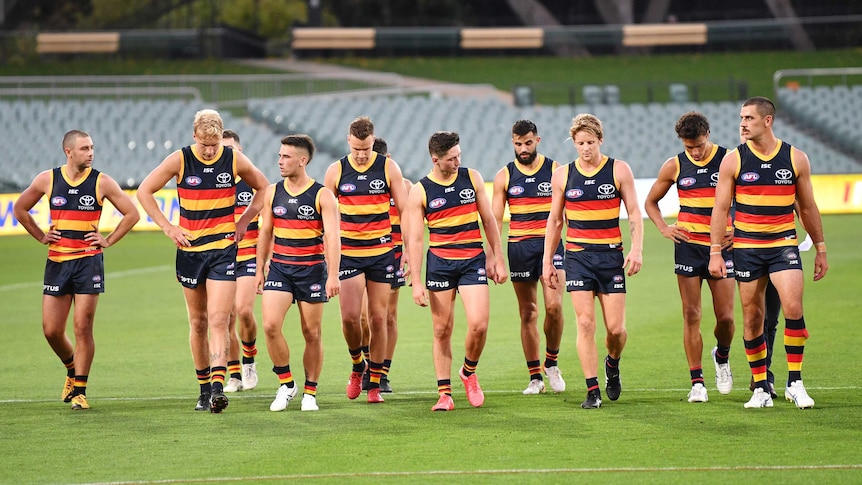 Adelaide Crows players look dejected as they walk off the field in front of empty stands