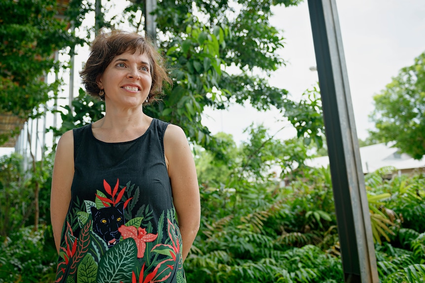 A woman looks to the distance in front of greenery.