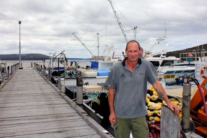 Man stands on a jetty next to commercial fishing boats