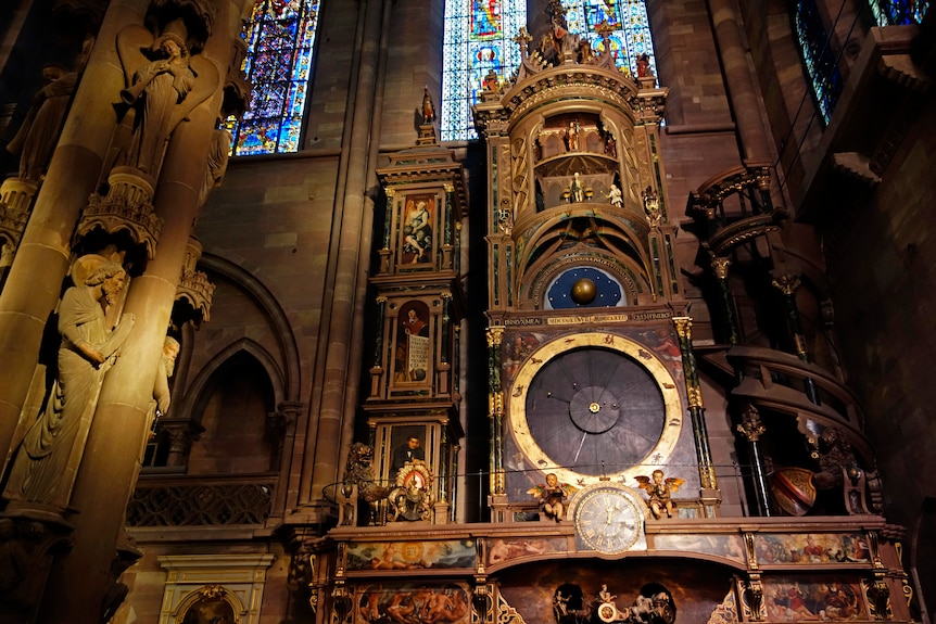 A large and highly ornate and detailed golden clock centrepiece, with the backdrop of internal cathedral walls.