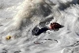A man lies on his back in foamy, rough water 