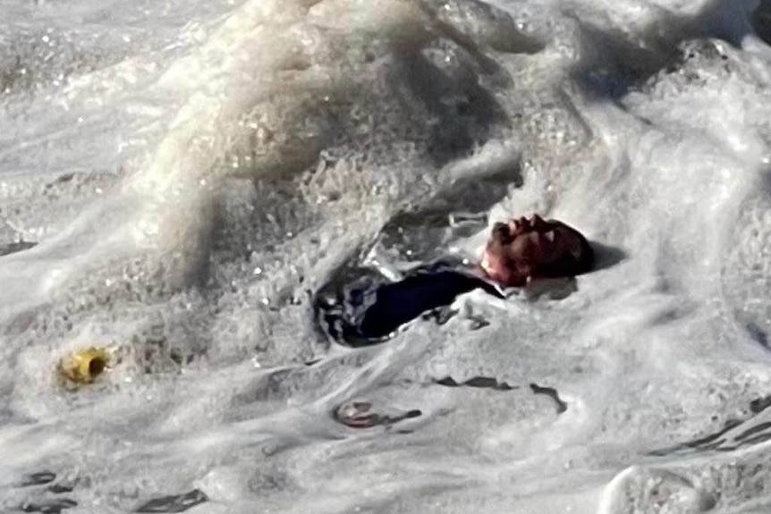 A man lies on his back in foamy, rough water 