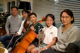 Two boys and a girl sit happily holding a viola, cello and trumpet. Their mum and dad sit next to them.