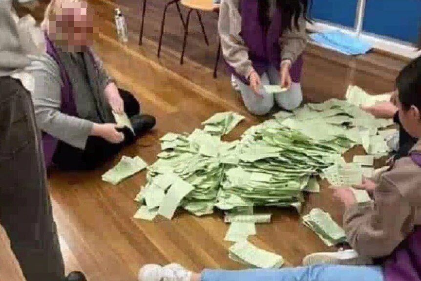 Voting staff count green ballot papers on the floor.