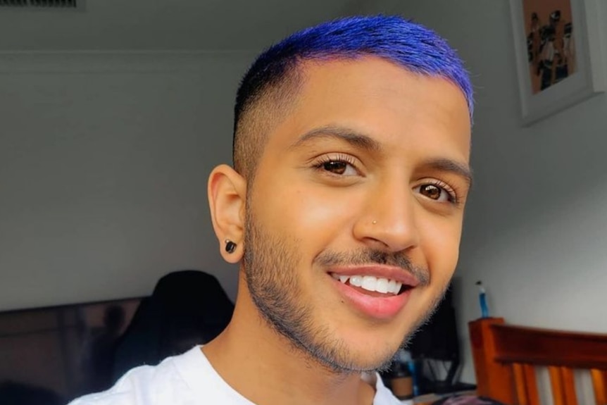 Photo of a young man with blue hair and a nose piercing looking happy.
