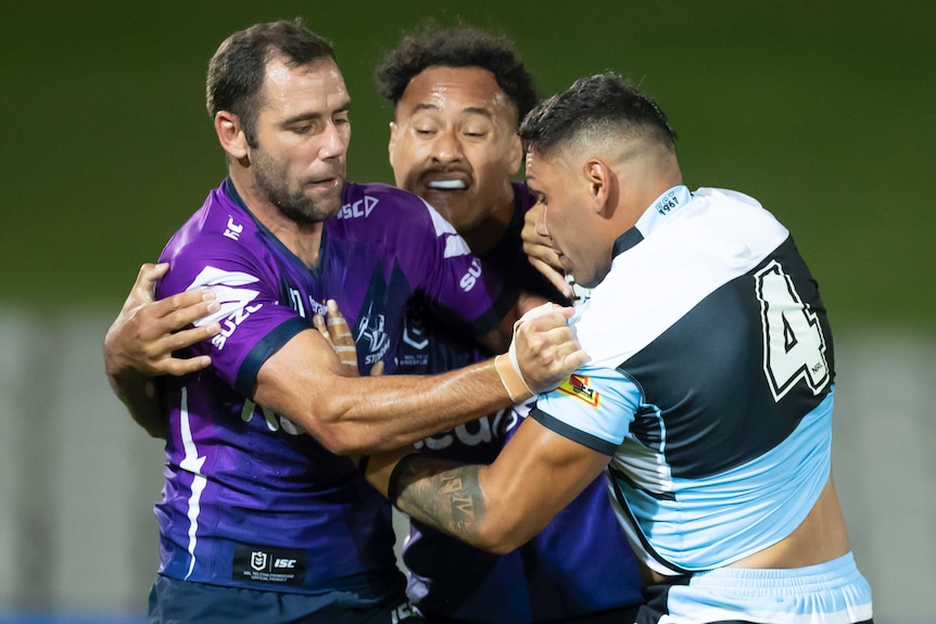 A Cronulla NRL players is tackled by two Melbourne Storm players.