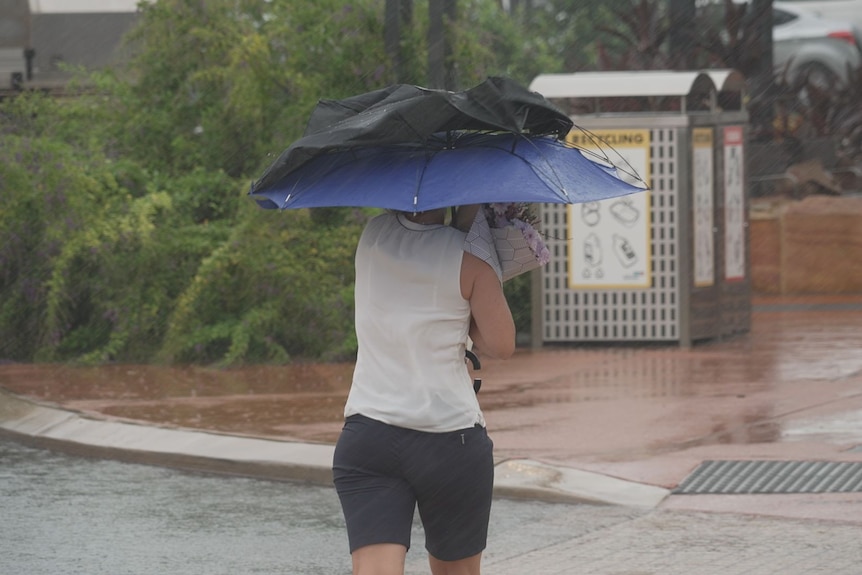 A woman takes cover under an umbrella as it rains in Broome.