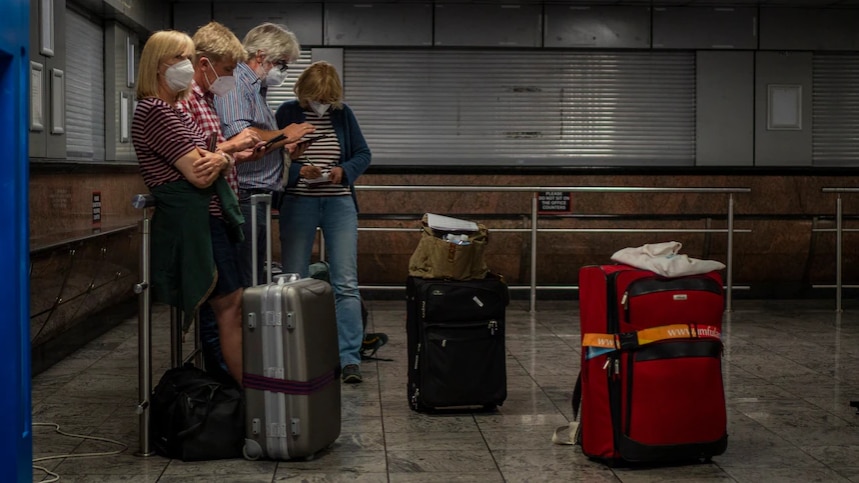 Four passengers with luggage wait at an empty transport station.