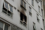 A window on a tall building with black streaks of smoke damage smeared across it.