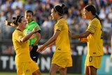 Three Matildas players celebrate scoring.