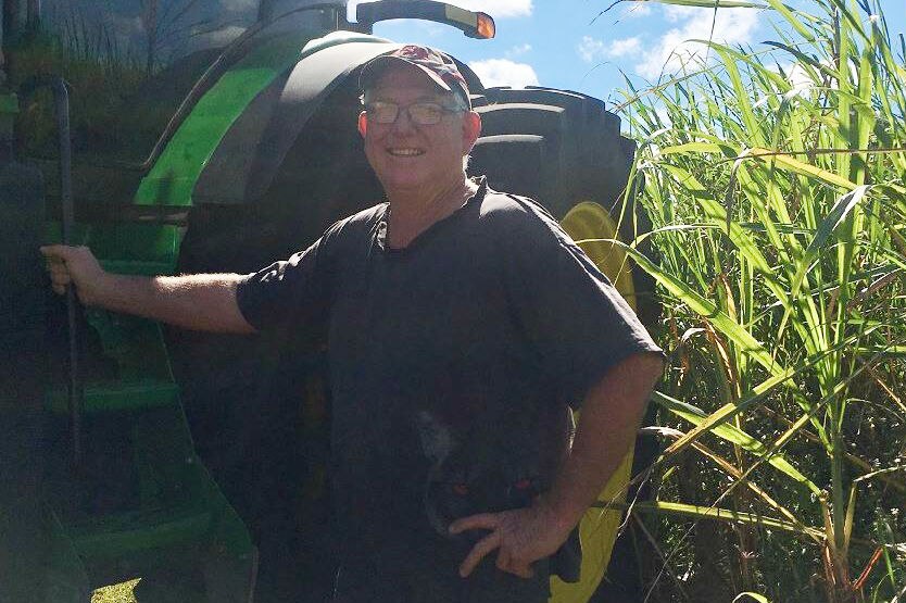 Cane farmer Tony Large stands beside a green tractor parked next to sugar cane.