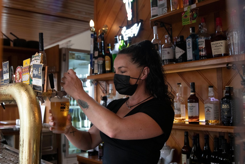 Woman with dark hair wearing a mask pouring a beer at a pub 