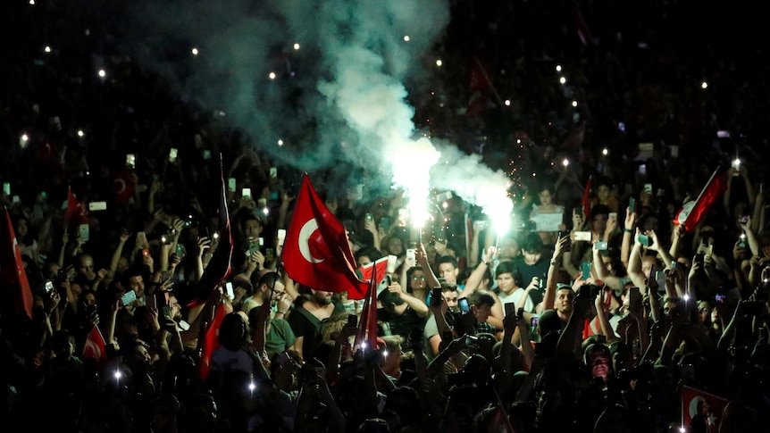 People on the street with Turkish flags and bright flares and smoke.