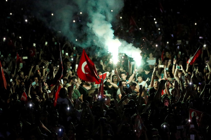 People on the street with Turkish flags and bright flares and smoke.