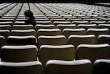 A sad looking older woman sitting alone amongst many empty seats
