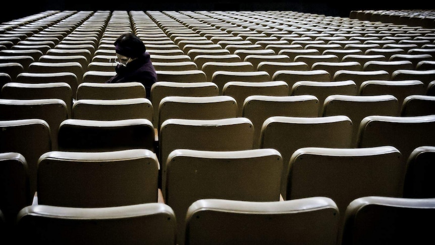 A sad looking older woman sitting alone amongst many empty seats