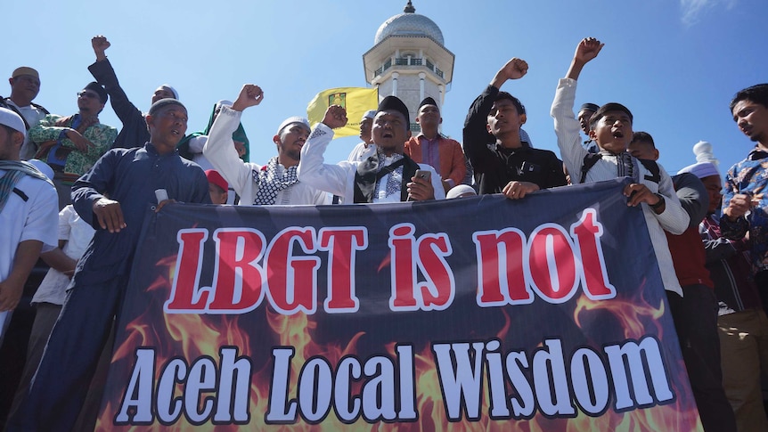 Anti-LGBT protestors stand behind large banner that says "LGBT is not Aceh Local Wisdom".