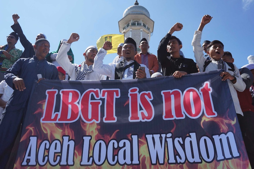 Anti-LGBT protestors stand behind a large banner that says "LGBT is not Aceh Local Wisdom".