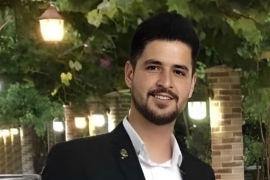 A man with dark hair and facial hair smiling in suit