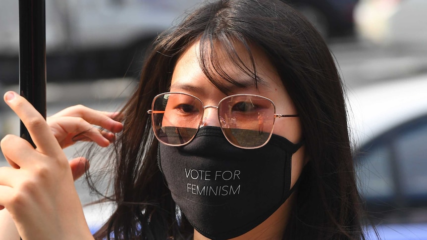 A South Korean women wearing a black mask that reads 'vote for feminism'.