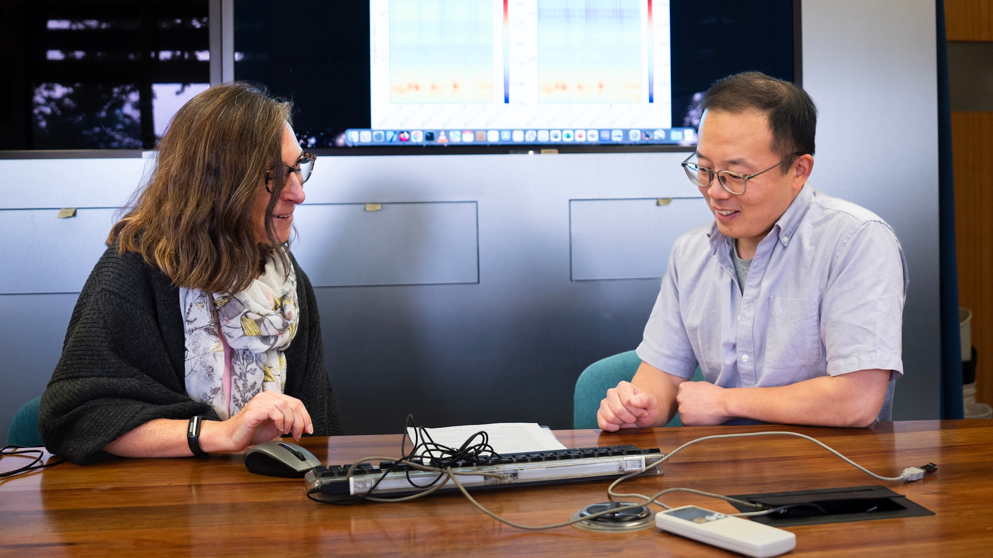 Dois cientistas estão sentados à mesa lendo uma folha de papel.