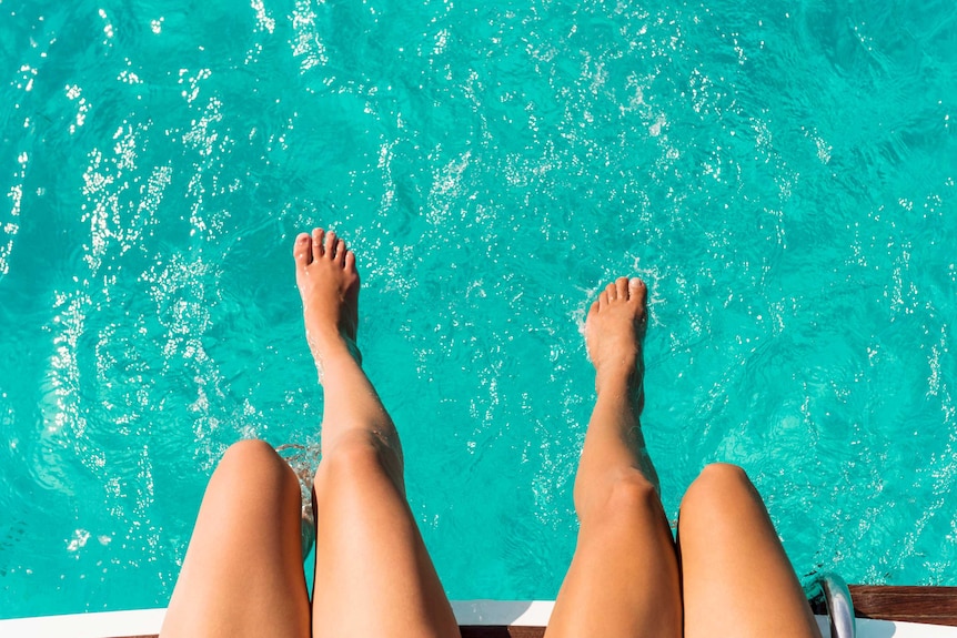 Two women dip their feet and legs into a pool