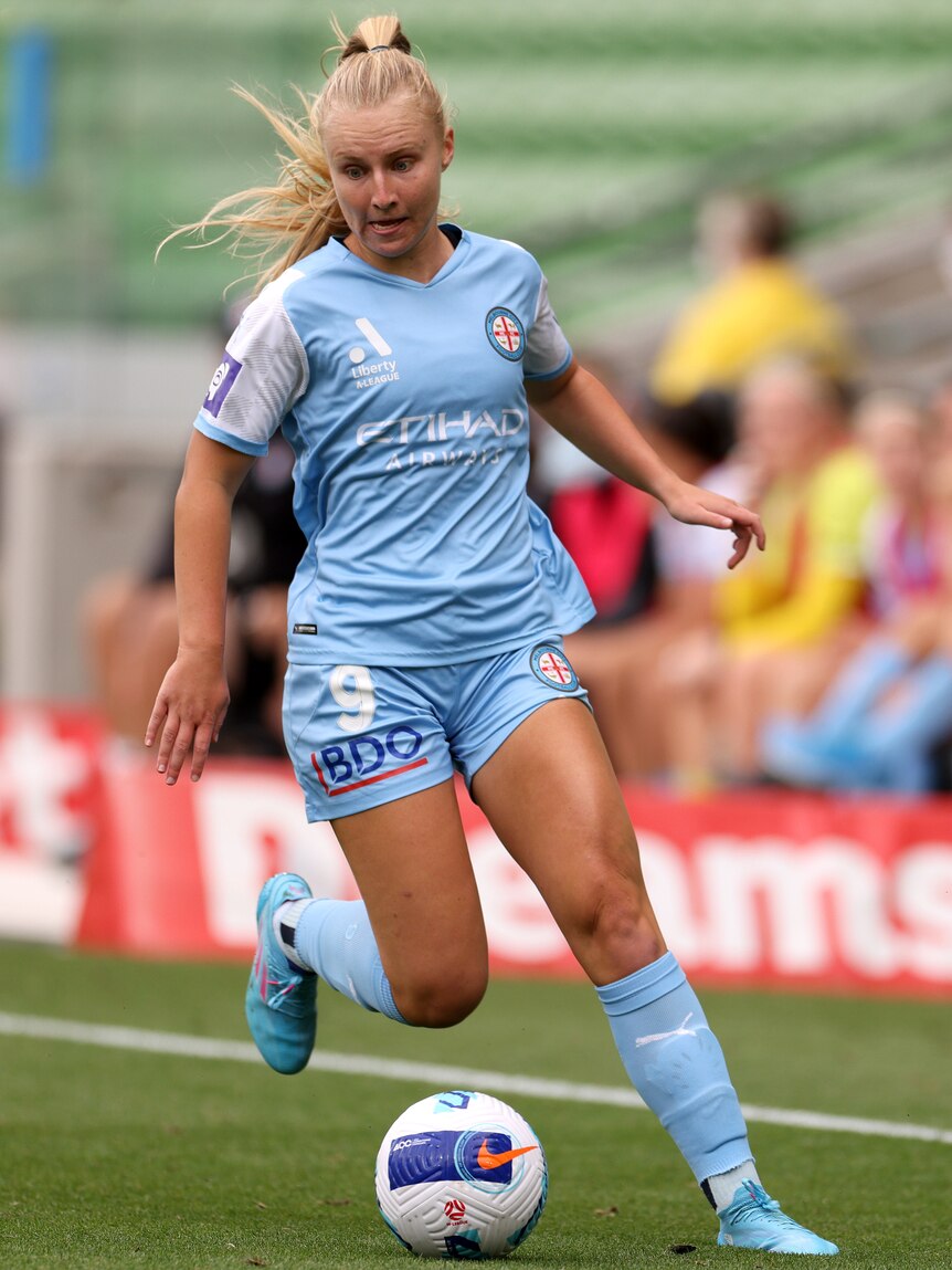 A soccer player wearing sky blue dribbles with the ball during a game