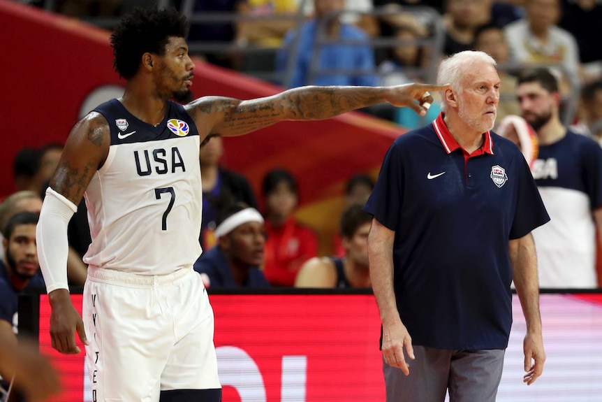 Marcus Smart points to something off camera as Gregg Popovic stands with his hands by his sides wearing a blue polo shirt