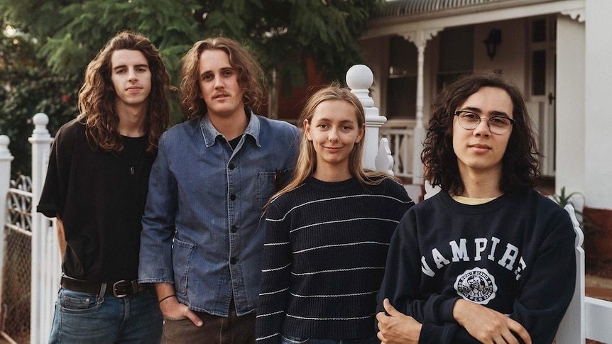 Photo of the band members of Spacey Jane standing in front of a white picket fence, house, and tree.