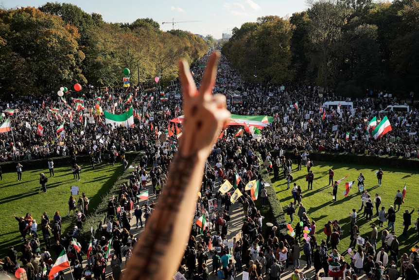 A crowd of people can be seen below as a person makes a gesture with their hand. 