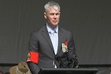 A man stands during this year's Anzac Day service in Albany. He's wearing a suit.